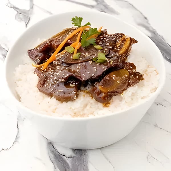 Korean Galbi-jjim (braised short ribs) over white rice, garnished with carrots, cilantro, and sesame seeds.