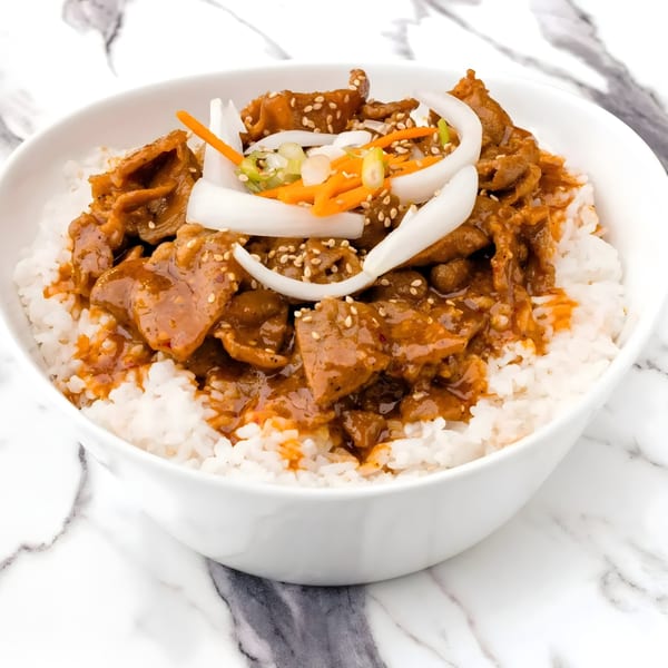 Arkanseoul's Korean bulgogi beef over white rice, garnished with onions, carrots, and sesame seeds.